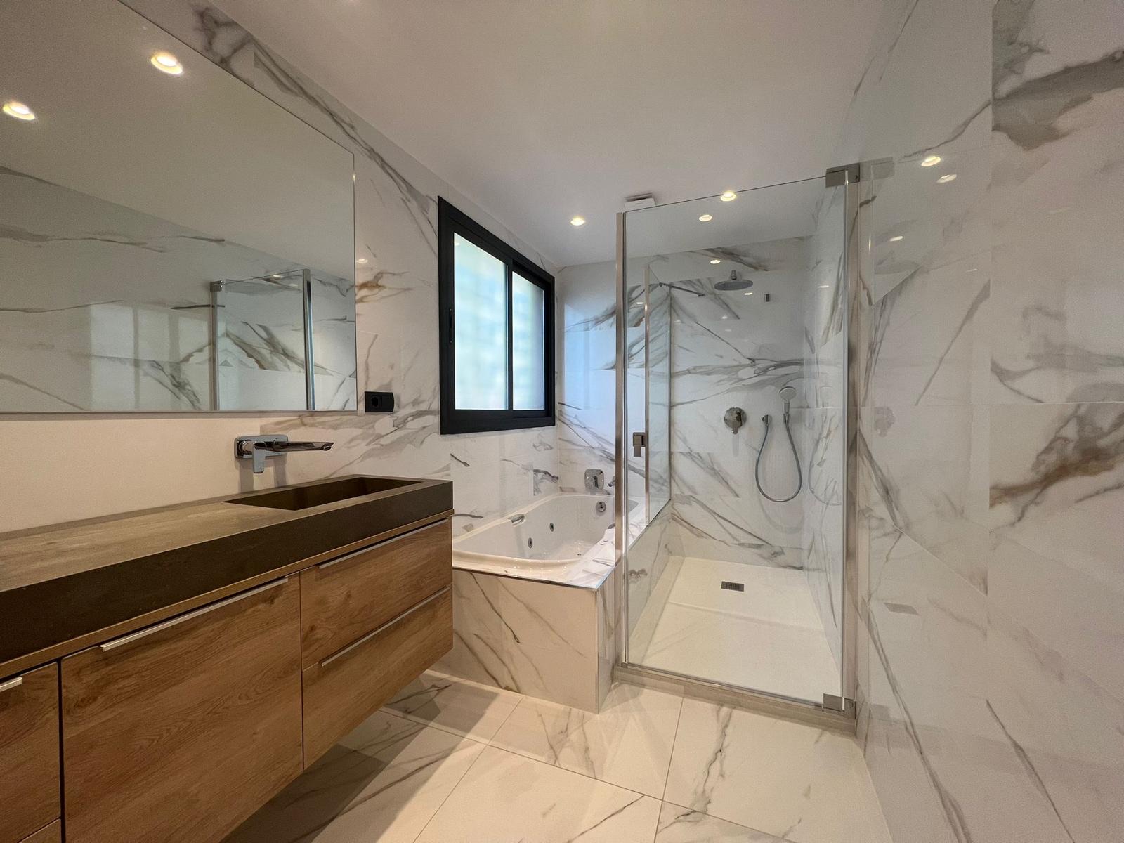 Baño reformado en mármol con mueble de madera